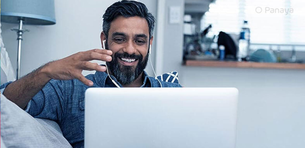 A bearded man with headphones in having a video chat with someone on a laptop and smiling
