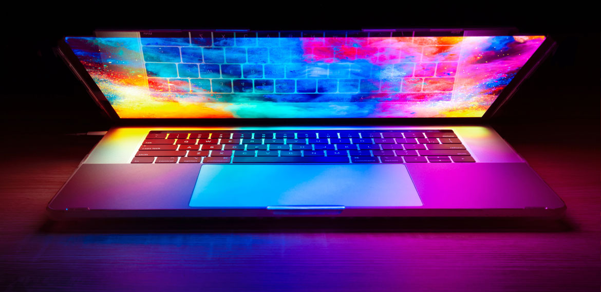 A laptop partially open with a colourful screensaver illuminating the keyboard
