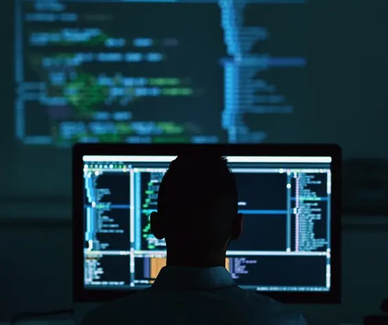 Person working at a computer with multiple monitors displaying code and system diagnostics on a dark screen.